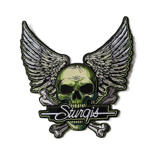 May include: An embroidered patch featuring a green skull with large, detailed grey wings extending upwards. Behind the skull are crossed grey bones. A black horizontal banner across the lower portion displays the white text Sturgis.