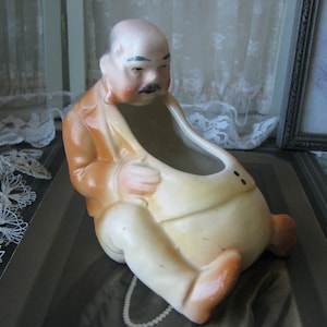 May include: A ceramic planter shaped like a man with a brown jacket and a white shirt. The planter has a large opening in the front for planting.