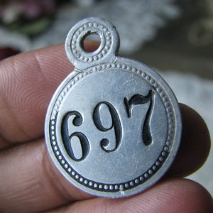 May include: A silver metal tag with a ring at the top and the number 697 printed in black.
