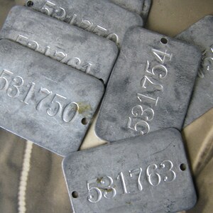 May include: Close-up of a stack of silver metal tags with different numbers, including 531750, 531763, and 531754.