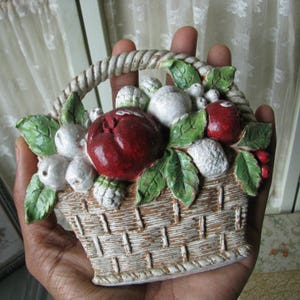 May include: A white ceramic basket filled with red and white fruit, with green leaves. The basket is hand-painted and has a rustic look.