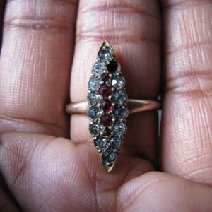 Puede incluir: Un anillo de oro con un dise&ntilde;o puntiagudo engastado con piedras preciosas transparentes y rojas.