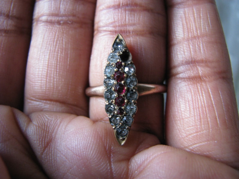 Puede incluir: Un anillo de oro con un dise&ntilde;o puntiagudo engastado con piedras preciosas transparentes y rojas.