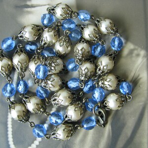 May include: A vintage necklace with white faux pearl beads and blue glass beads. The pearl beads are encased in ornate silver-toned metal settings.