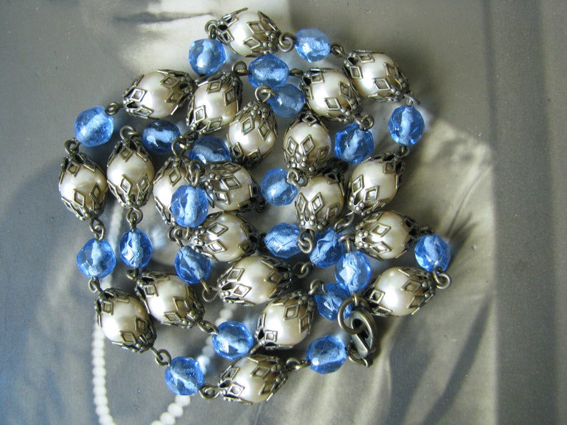 May include: A vintage necklace with white faux pearl beads and blue glass beads. The pearl beads are encased in ornate silver-toned metal settings.