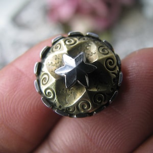 Puede incluir: Un anillo de plata y oro con un diseño de estrella de cinco puntas. La estrella está hecha de plata y está engastada en un anillo de oro. El anillo está decorado con un patrón de espiral.