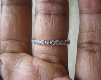 Puede incluir: Un anillo de banda de plata con una fila de pequeñas piedras preciosas transparentes.