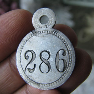 May include: A silver metal tag with a circular design and the number 286 embossed on the front. The tag has a small loop at the top for attaching.