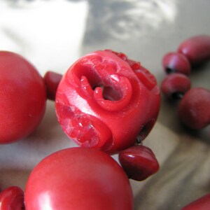 Peut inclure: Un collier de perles rouges avec des d&eacute;tails sculpt&eacute;s sur les perles. Le collier est compos&eacute; de perles rondes avec une finition brillante.