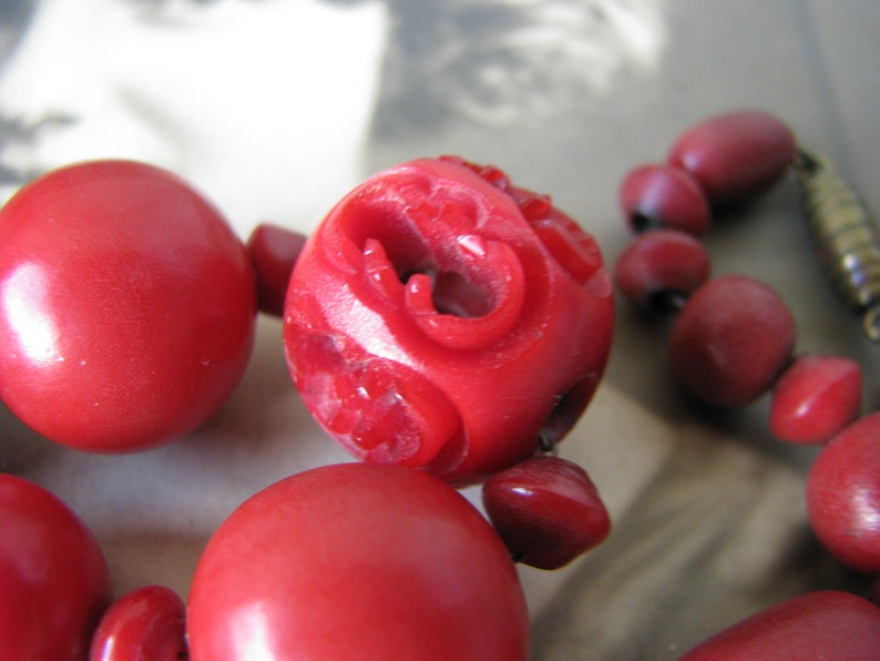 Peut inclure: Un collier de perles rouges avec des d&eacute;tails sculpt&eacute;s sur les perles. Le collier est compos&eacute; de perles rondes avec une finition brillante.
