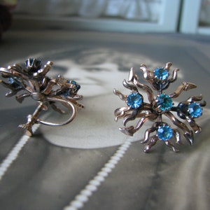 May include: A pair of gold tone clip-on earrings with blue rhinestones set in a floral design.