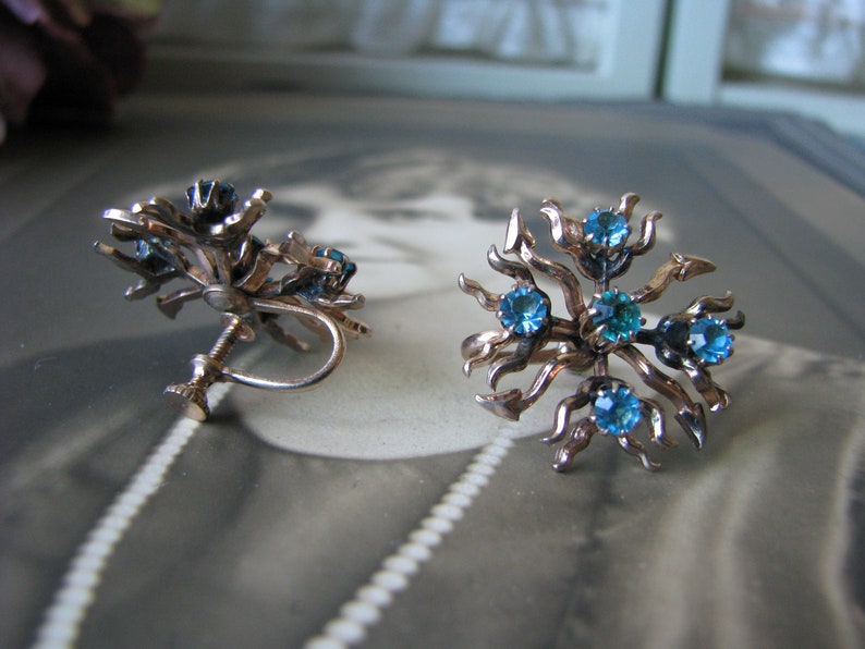 May include: A pair of gold tone clip-on earrings with blue rhinestones set in a floral design.