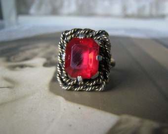 May include: A red gemstone ring with a gold and silver rope-like setting.