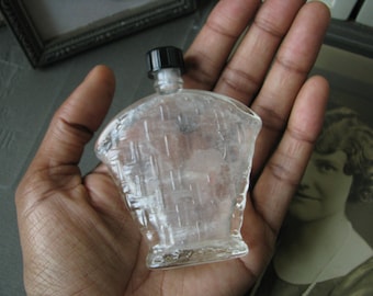 May include: A clear glass bottle with a black plastic cap and a textured surface. The bottle is empty and has a slightly rounded shape.
