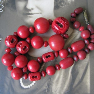 Peut inclure: Un collier de perles rouges avec des perles en bois sculpt&eacute;es. Le collier est compos&eacute; de deux rangs de perles, un rang est plus grand que l'autre. Les perles sont d'une couleur rouge fonc&eacute; et ont une finition brillante.