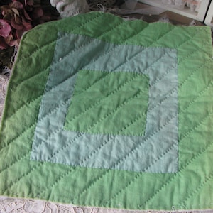 May include: A green and blue quilted square with a diamond pattern. The square is made of fabric and has a frayed edge.