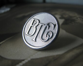 May include: A silver-toned metal button with the letters "BTC" embossed on it.