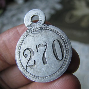 May include: A silver metal tag with a circular shape and a hole at the top. The tag has a beaded border and the number "270" is engraved in the center.