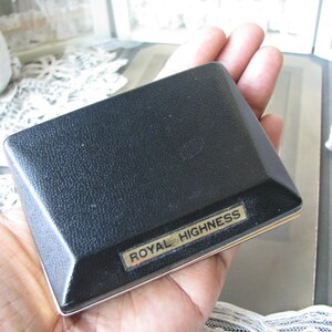 May include: A black rectangular box with a gold trim and the words "Royal Highness" printed on the front.