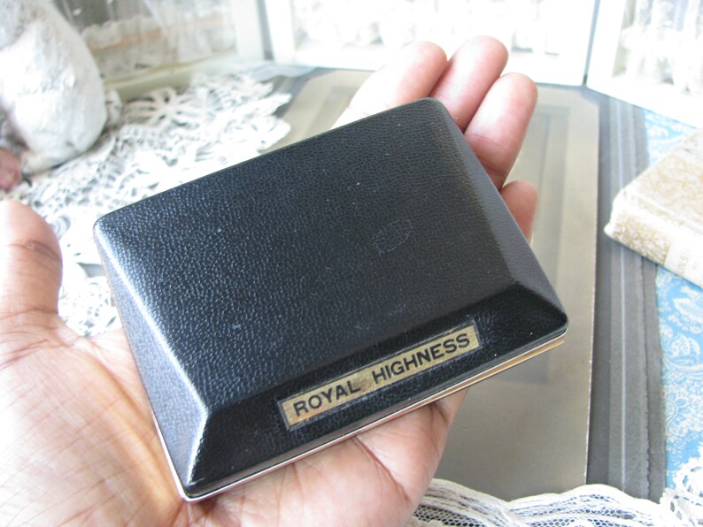 May include: A black rectangular box with a gold trim and the words "Royal Highness" printed on the front.