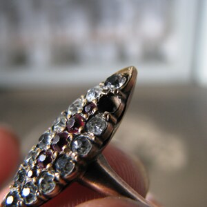 Puede incluir: Un anillo de oro con un dise&ntilde;o puntiagudo, engastado con un grupo de piedras preciosas rojas y transparentes.
