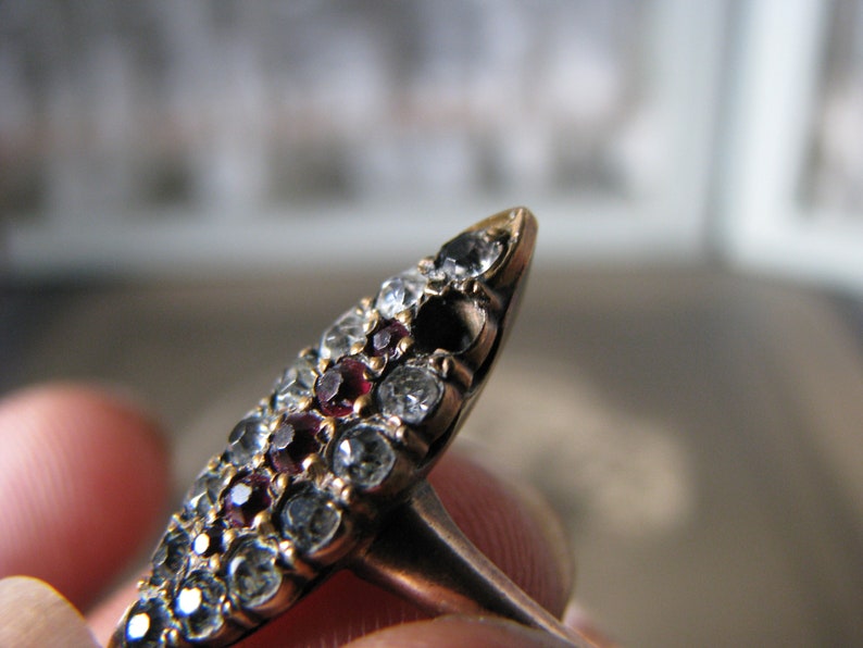Puede incluir: Un anillo de oro con un dise&ntilde;o puntiagudo, engastado con un grupo de piedras preciosas rojas y transparentes.