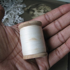 Op de afbeelding: Een houten spoel met witte draad, vastgehouden in een hand.