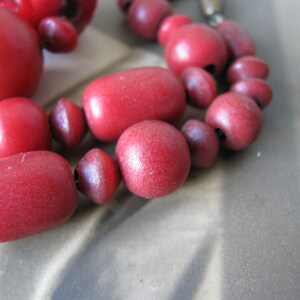 Peut inclure: Gros plan d'un collier de perles en bois rouge. Les perles sont de diff&eacute;rentes tailles et formes, et le collier est enfil&eacute; sur un cordon fonc&eacute;.
