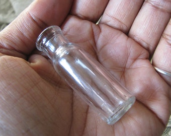 Puede incluir: Una botella de vidrio transparente con fondo redondeado y una abertura ligeramente acampanada. La botella está vacía y parece ser vintage.