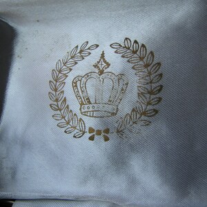 May include: A white fabric box with a gold crown and laurel wreath design.