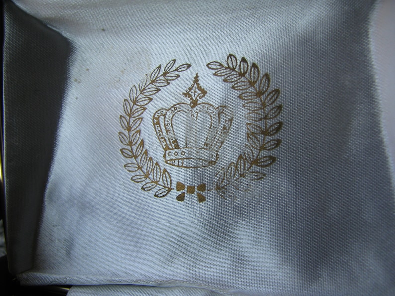 May include: A white fabric box with a gold crown and laurel wreath design.