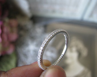 Puede incluir: Una fina banda de plata con una fila de pequeños diamantes transparentes que rodean el anillo.