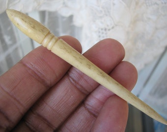 May include: A long, thin, off-white bone knitting needle with a rounded tip and a decorative band near the tip.