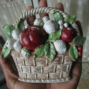 May include: A white ceramic basket filled with red and white fruit, with green leaves. The basket is decorated with a rope-like trim.