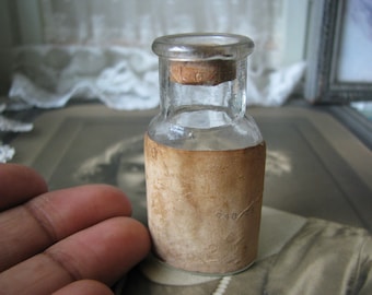 May include: A small, clear glass bottle with a cork stopper and a brown paper label. The label has the number "748" printed on it.