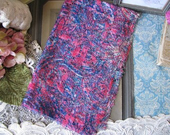 Pode incluir: Um close-up de um tecido rosa e azul com textura de renda. O tecido tem um aspecto desgastado, com bordas desfiadas e uma aparência desbotada.