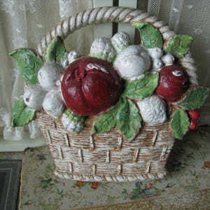 May include: A white ceramic basket filled with red and white fruit. The basket has a woven design and is decorated with green leaves.