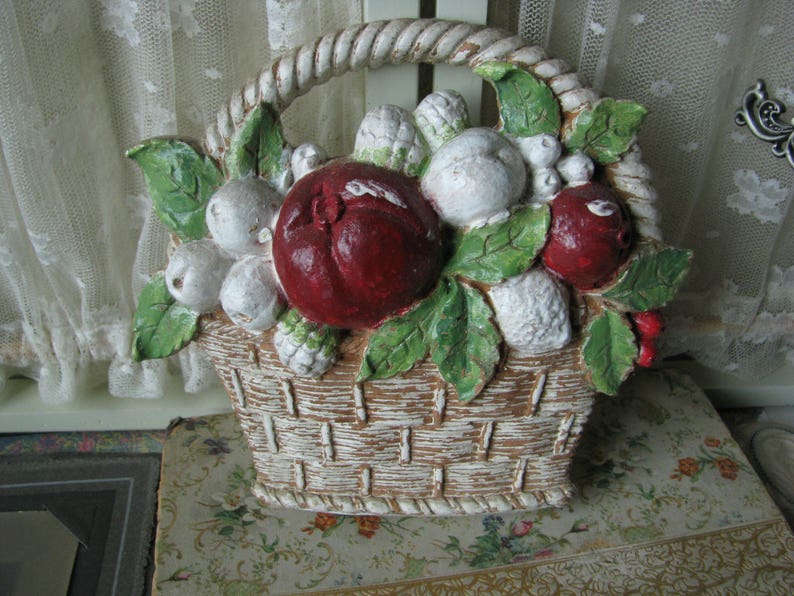 May include: A white ceramic basket filled with red and white fruit. The basket has a woven design and is decorated with green leaves.