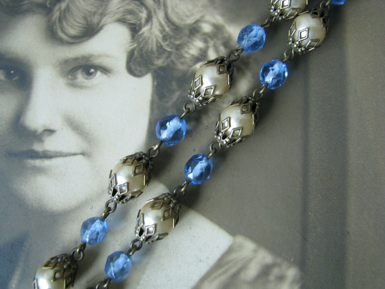 May include: A vintage necklace with blue glass beads and white pearl-like beads in ornate metal settings.