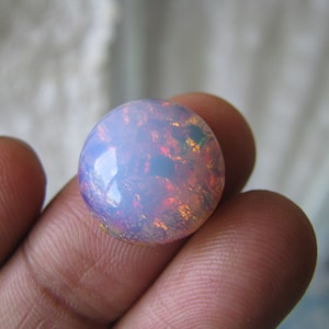 Peut inclure: Un cabochon d'opale ronde et blanche avec des reflets irisés de rose, d'orange et de vert. L'opale est sertie dans une bélière en argent.