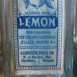 May include: A vintage glass bottle with a blue and white label that reads "ALCOHOL 90% LEMON FOR FLAVORING ICE CREAM, CUSTARDS JELLIES, PASTRY & C. GARDINER DRUG CO. W. A. Burdick, Mgr. Gardiner, Oregon"