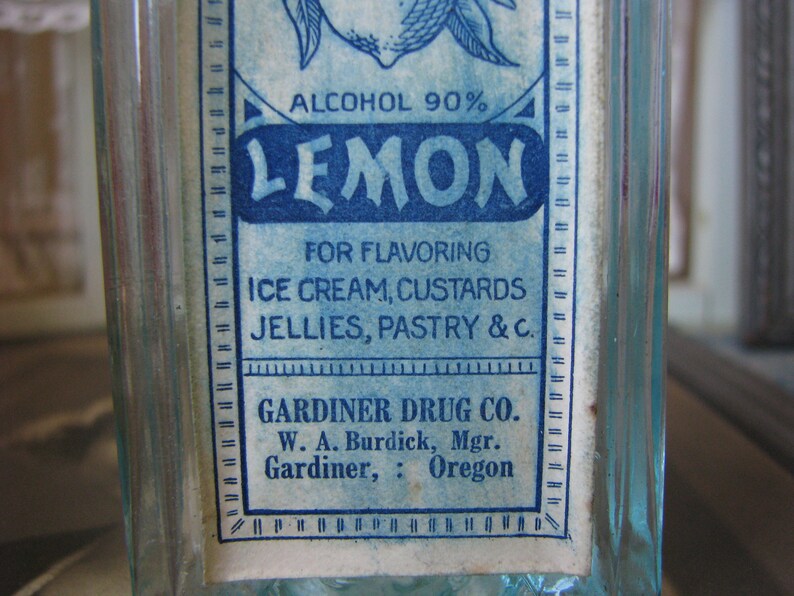 May include: A vintage glass bottle with a blue and white label that reads "ALCOHOL 90% LEMON FOR FLAVORING ICE CREAM, CUSTARDS JELLIES, PASTRY & C. GARDINER DRUG CO. W. A. Burdick, Mgr. Gardiner, Oregon"