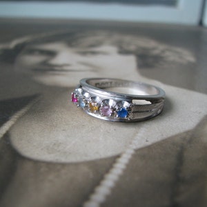 May include: A silver ring with a row of colorful gemstones. The ring has a textured band and a smooth, polished finish.
