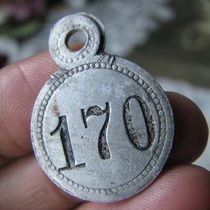 May include: A silver metal tag with a circular design and the number 170 embossed on it. The tag has a loop at the top for attaching.