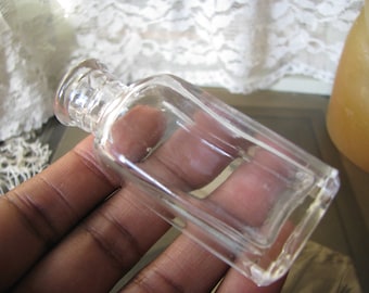 Puede incluir: Una botella de vidrio transparente con una parte superior redondeada y un cuerpo rectangular. La botella está vacía y parece ser vintage.