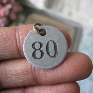 May include: A silver metal tag with the number 80 printed in black. The tag has a small brass loop at the top.