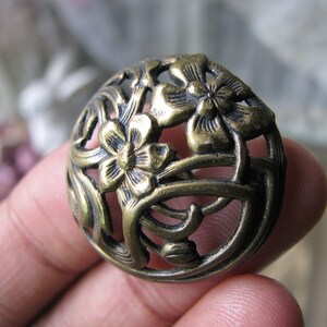 Puede incluir: Un adorno de metal dorado con un delicado diseño floral. El adorno tiene una forma circular con intrincados recortes y detalles florales en relieve.