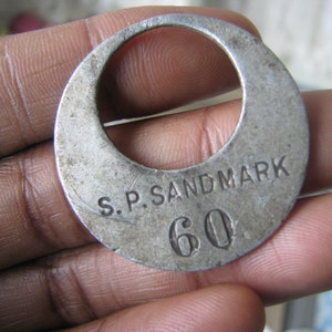 May include: A silver metal token with the text "S.P. SANDMARK 60" engraved on it.