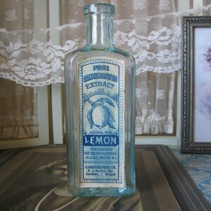 May include: A vintage glass bottle with a blue and white label that reads "Pure Concentrated Extract of Lemon, Alcohol 90%". The label also includes instructions for using the extract for flavoring ice cream, custards, jellies, pastry, and other foods. The bottle is made by Gardiner Drug Co. in Gardiner, Oregon.