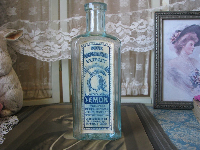 May include: A vintage glass bottle with a blue and white label that reads "Pure Concentrated Extract of Lemon, Alcohol 90%". The label also includes instructions for using the extract for flavoring ice cream, custards, jellies, pastry, and other foods. The bottle is made by Gardiner Drug Co. in Gardiner, Oregon.